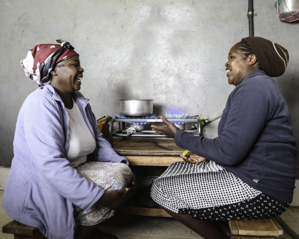 Two African ladies talking whilst sitting next to gas stove cooking
