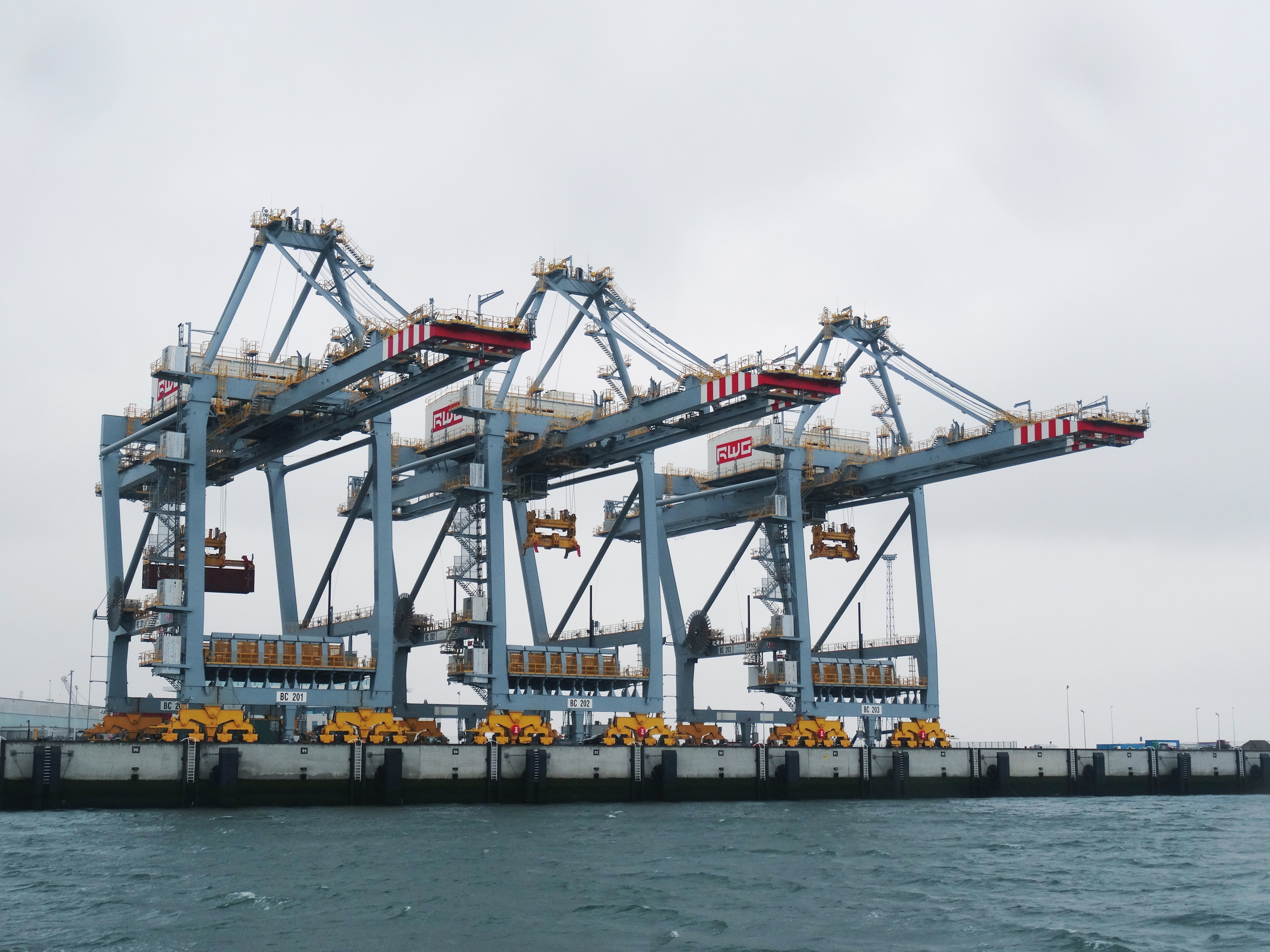 Three large freight cranes on the docks next to sea