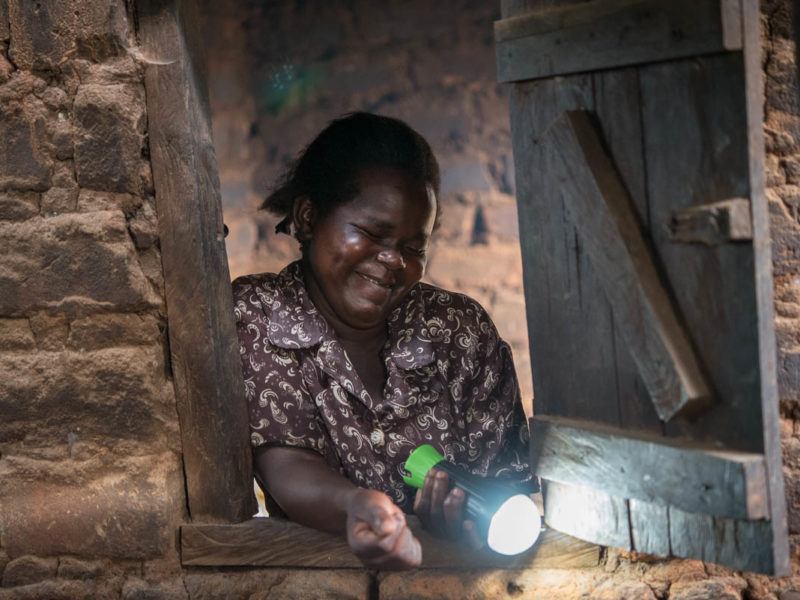 African lady shining solar torch through window opening