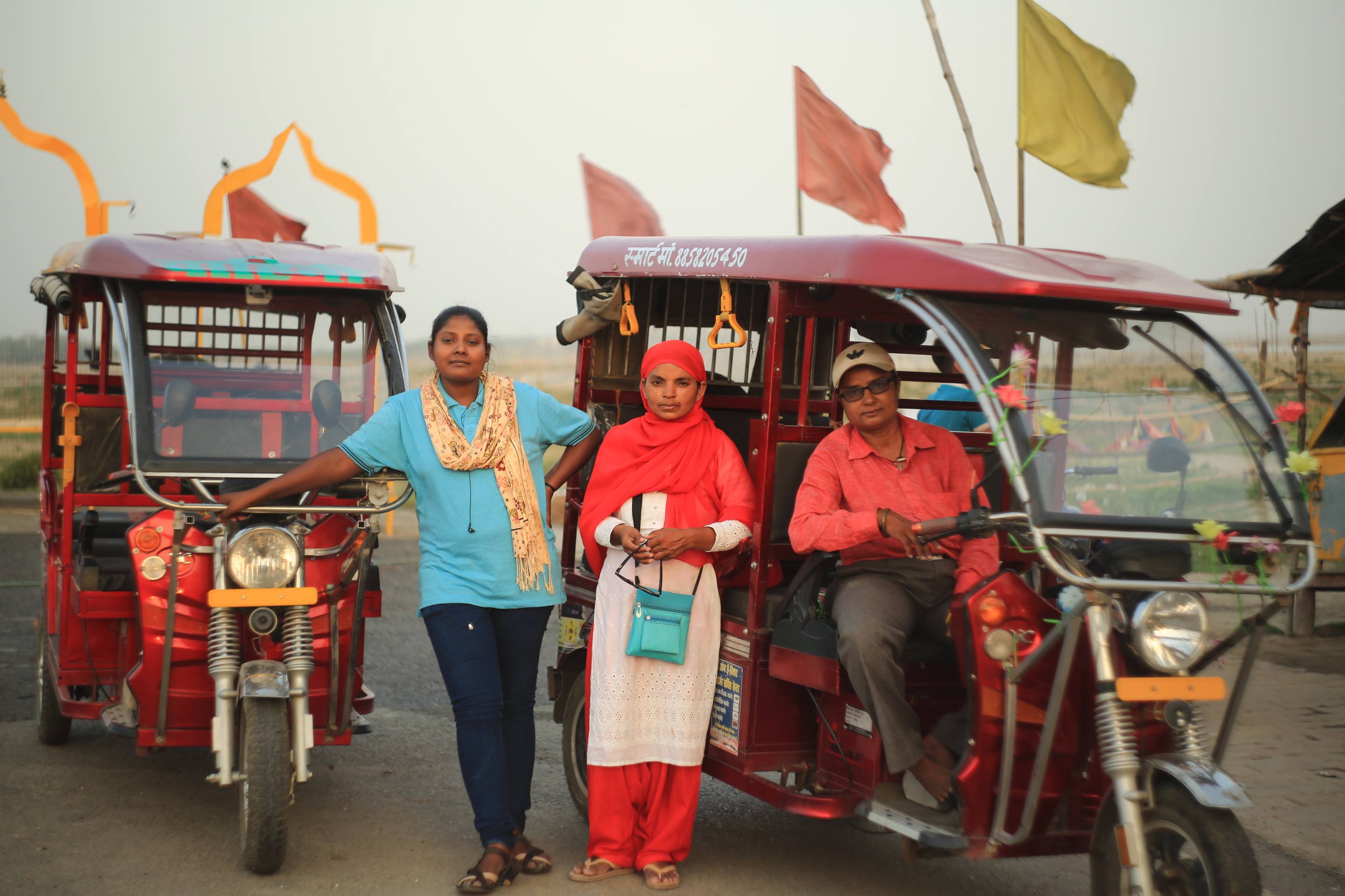 Three female e-rickshaw drivers in front of their rickshaws