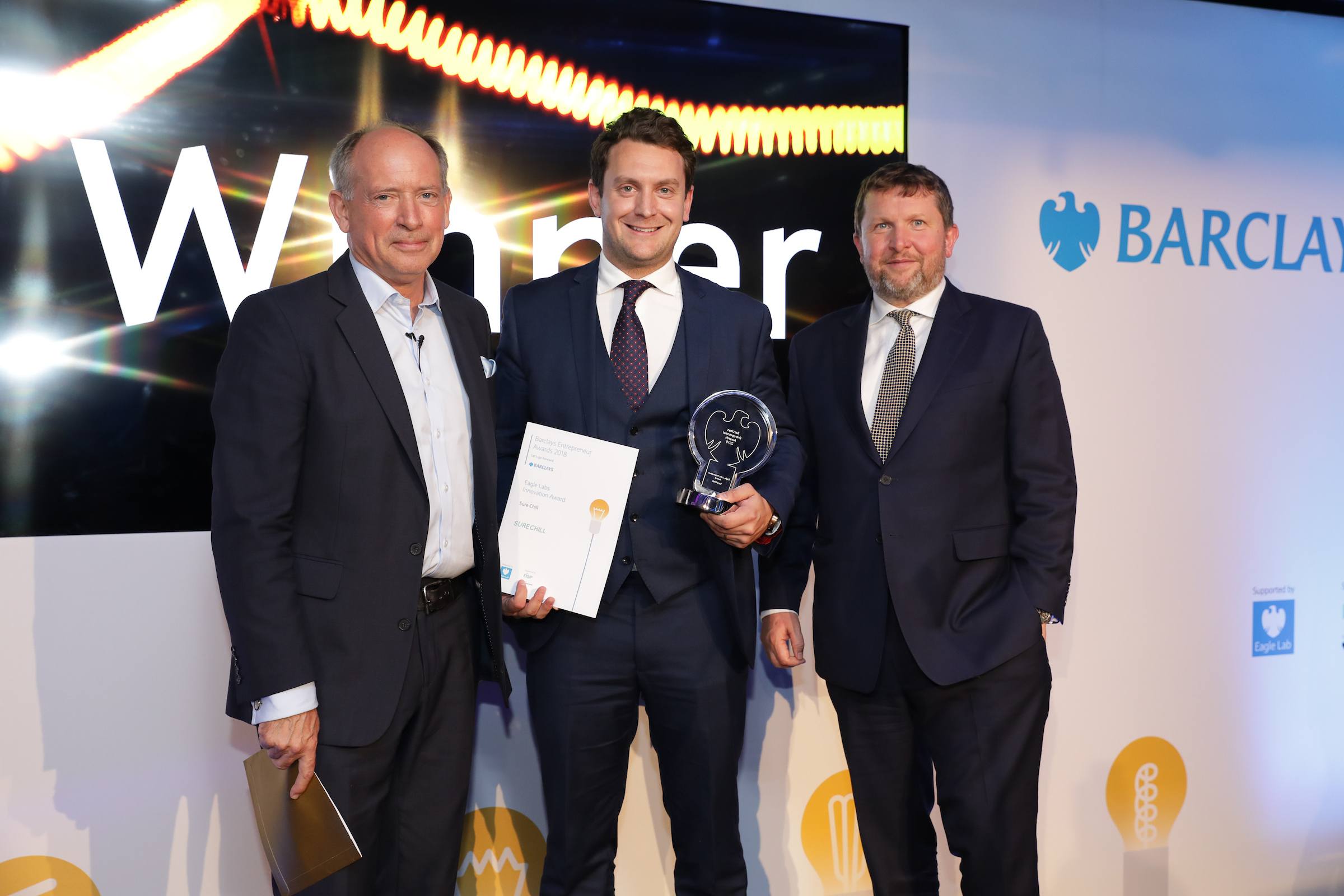 Three men facing camera one in centre holding awards