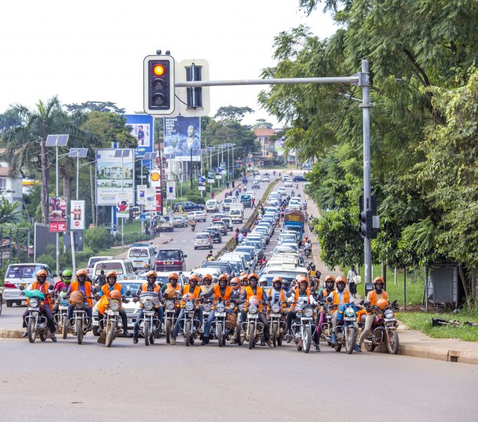 A line of motorbike taxi drivers wait at traffic lights at a city junction